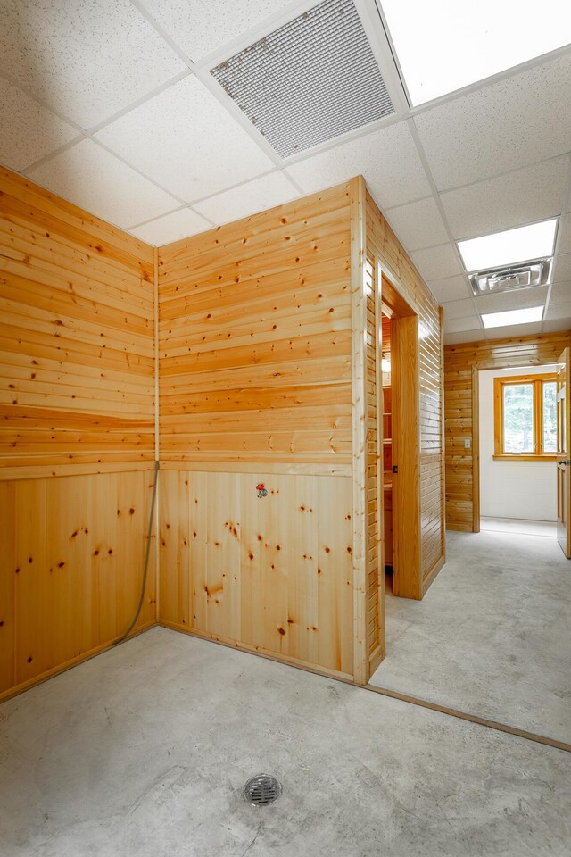 interior space with a paneled ceiling, concrete floors, and wooden walls