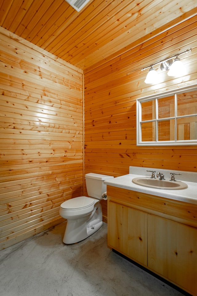 bathroom featuring concrete floors, vanity, toilet, and wood walls