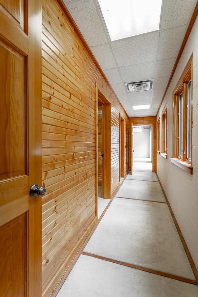 hall featuring concrete floors, wood walls, and a drop ceiling