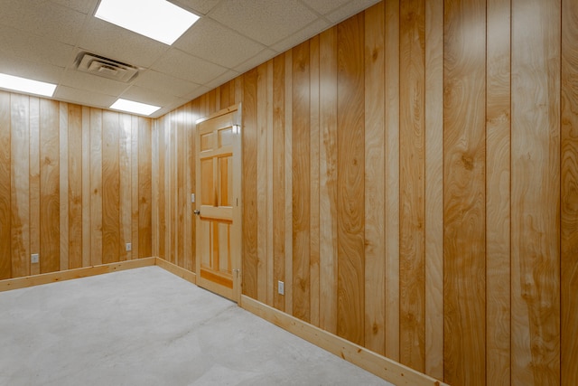 basement featuring a paneled ceiling and wood walls