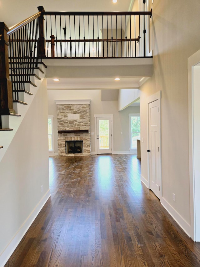 unfurnished living room featuring a high ceiling, wood-type flooring, and a stone fireplace