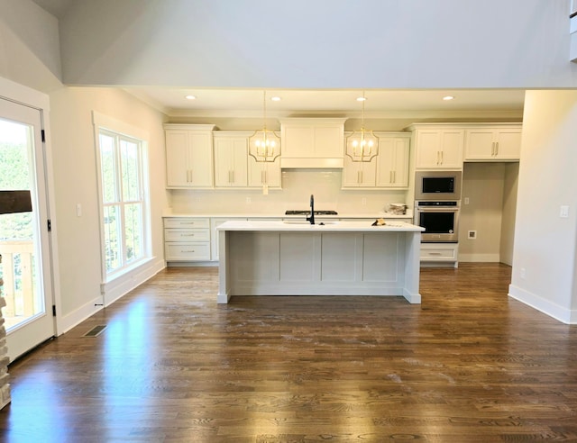 kitchen with dark wood-type flooring, white cabinets, appliances with stainless steel finishes, and a center island with sink