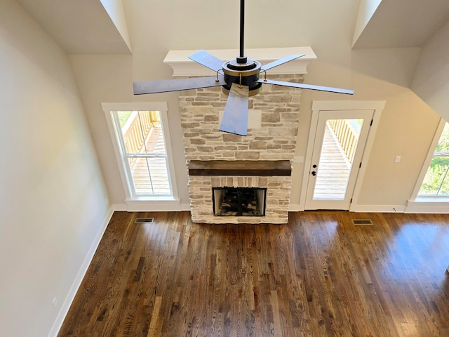 unfurnished living room featuring dark wood-type flooring, ceiling fan, and a stone fireplace