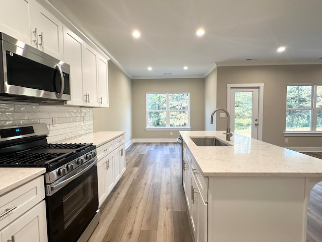 kitchen with white cabinets, appliances with stainless steel finishes, light wood-type flooring, and a kitchen island with sink