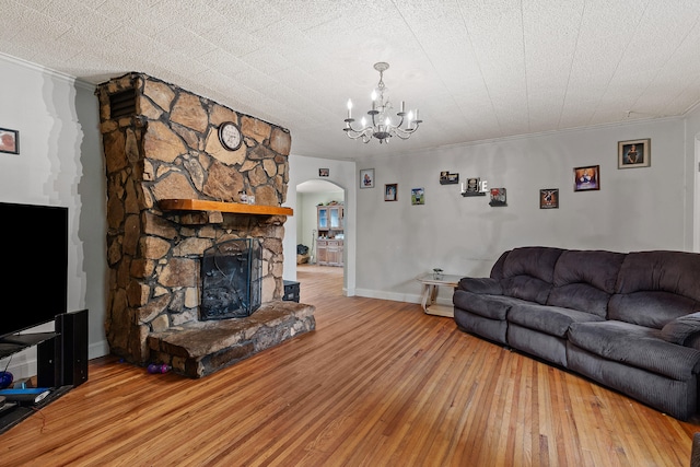 living room featuring an inviting chandelier, light hardwood / wood-style floors, ornamental molding, and a stone fireplace