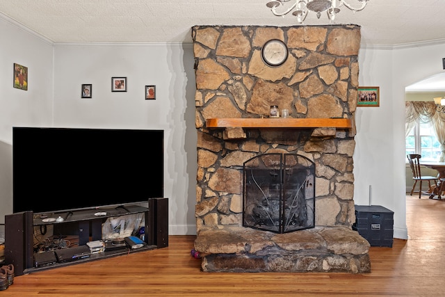 living room featuring hardwood / wood-style flooring, ornamental molding, a notable chandelier, and a stone fireplace