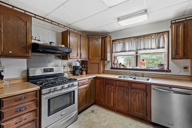 kitchen with appliances with stainless steel finishes, a paneled ceiling, sink, and range hood