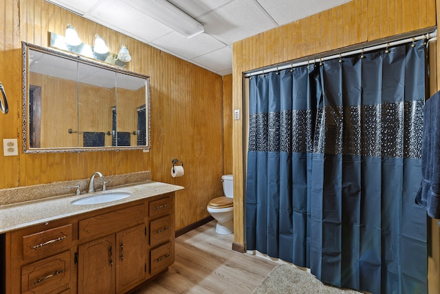 bathroom featuring toilet, hardwood / wood-style floors, wooden walls, vanity, and a paneled ceiling