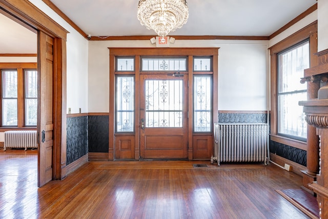 foyer with crown molding, dark wood-type flooring, radiator, and a chandelier