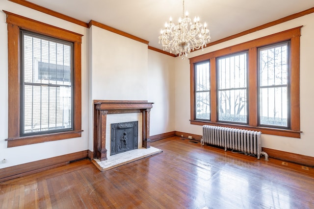 unfurnished living room with radiator heating unit, a wealth of natural light, an inviting chandelier, and dark hardwood / wood-style floors