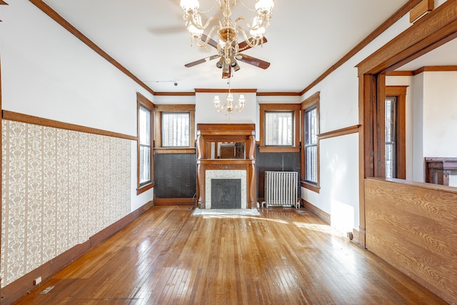 unfurnished living room featuring ceiling fan with notable chandelier, wood-type flooring, radiator heating unit, and crown molding