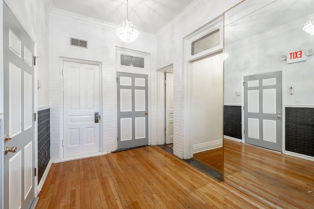 foyer entrance with brick wall, ornamental molding, wood-type flooring, and a notable chandelier