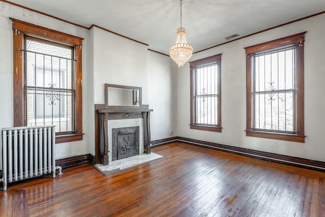 unfurnished living room featuring ornamental molding, radiator, dark wood-type flooring, and a notable chandelier