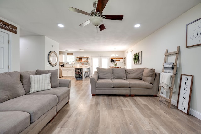 living room featuring light wood-type flooring and ceiling fan with notable chandelier