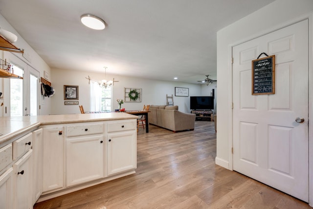 kitchen with white cabinets, light hardwood / wood-style flooring, decorative light fixtures, ceiling fan with notable chandelier, and kitchen peninsula