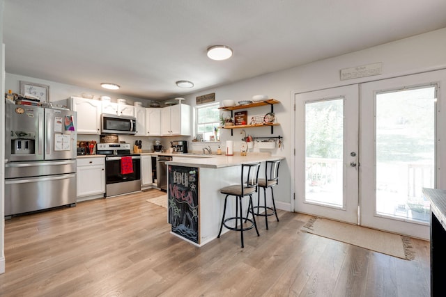 kitchen with appliances with stainless steel finishes, light hardwood / wood-style flooring, kitchen peninsula, and a kitchen bar