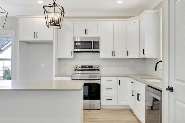 kitchen with light hardwood / wood-style flooring, a notable chandelier, appliances with stainless steel finishes, sink, and white cabinets