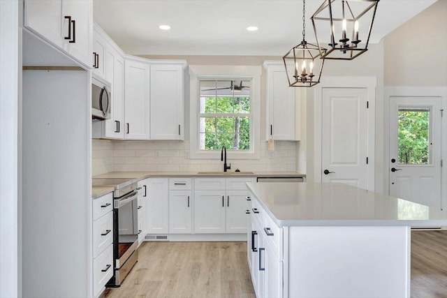 kitchen with light hardwood / wood-style flooring, stainless steel appliances, a chandelier, sink, and a kitchen island