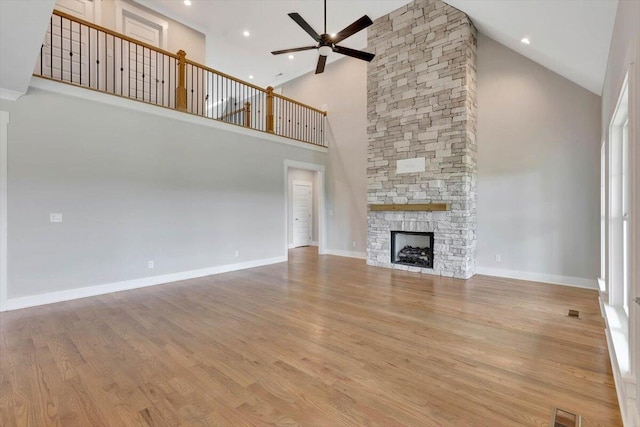 unfurnished living room featuring wood-type flooring, ceiling fan, a stone fireplace, and high vaulted ceiling