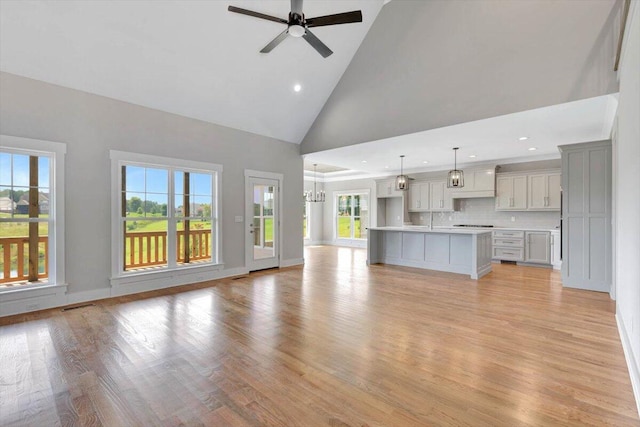 unfurnished living room with high vaulted ceiling, ceiling fan with notable chandelier, and light hardwood / wood-style flooring