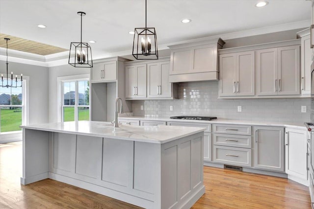 kitchen featuring a kitchen island with sink, light hardwood / wood-style flooring, a tray ceiling, and light stone countertops