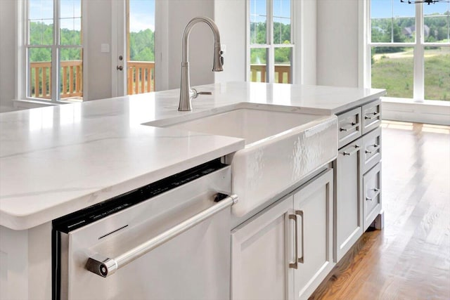 kitchen featuring dishwasher, plenty of natural light, light stone countertops, and light hardwood / wood-style floors