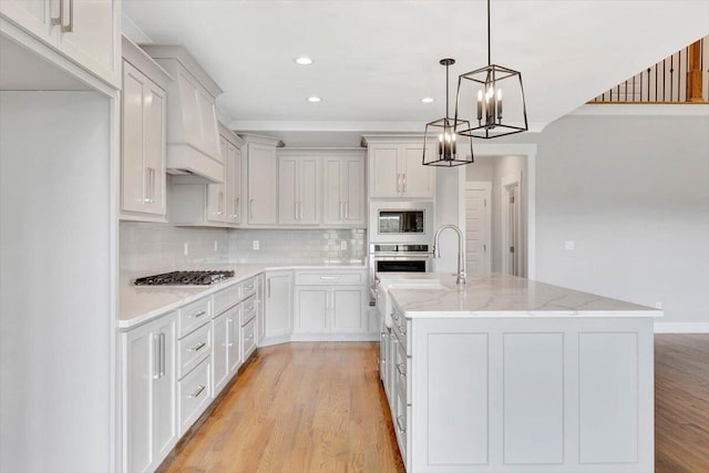 kitchen featuring light wood-type flooring, light stone countertops, stainless steel appliances, and an island with sink