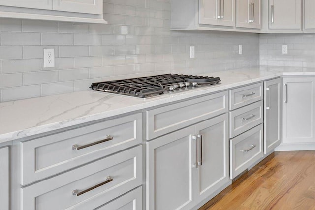 kitchen featuring stainless steel gas stovetop, light stone countertops, light hardwood / wood-style floors, and decorative backsplash