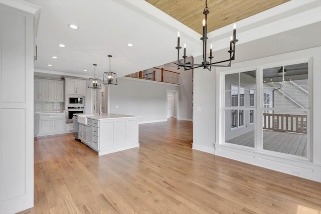 kitchen with oven, pendant lighting, light hardwood / wood-style floors, a kitchen island with sink, and white microwave