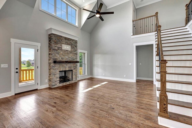 unfurnished living room with crown molding, ceiling fan, dark hardwood / wood-style floors, a stone fireplace, and high vaulted ceiling