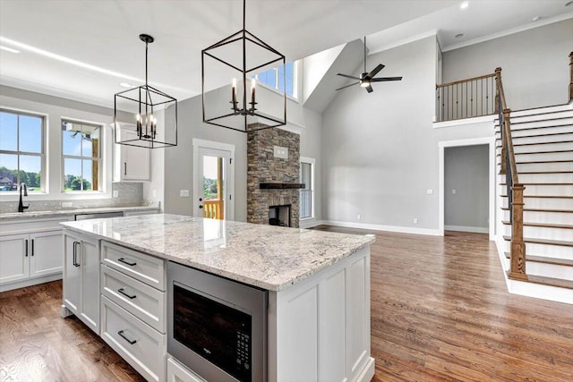 kitchen with black microwave, ceiling fan with notable chandelier, a stone fireplace, and white cabinetry