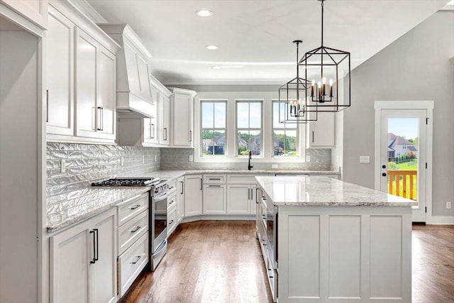 kitchen with a kitchen island, light stone countertops, dark wood-type flooring, white cabinetry, and stainless steel gas stove