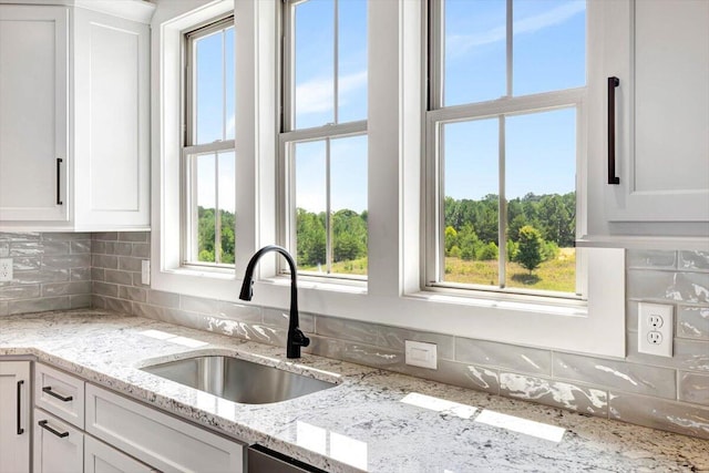 kitchen with white cabinets, light stone countertops, and sink