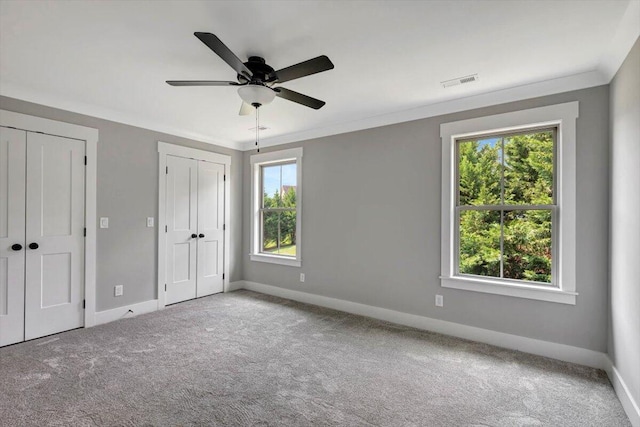 unfurnished bedroom featuring crown molding, ceiling fan, light carpet, and multiple closets