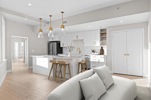 kitchen with white cabinets, stainless steel refrigerator with ice dispenser, light hardwood / wood-style flooring, and pendant lighting