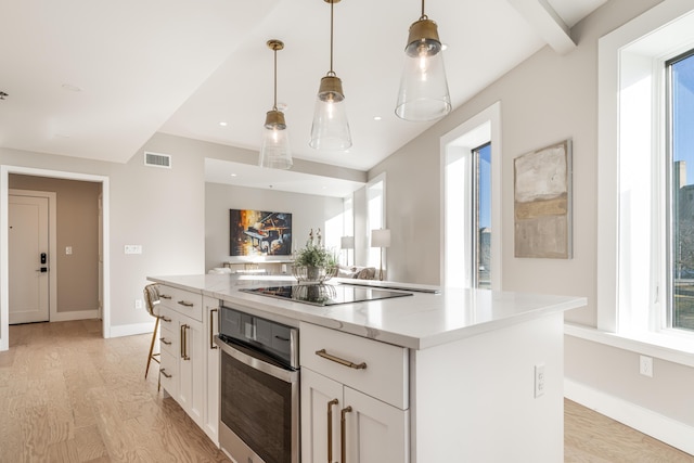 kitchen featuring a center island, oven, hanging light fixtures, light hardwood / wood-style flooring, and white cabinetry