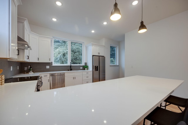 kitchen with hanging light fixtures, a kitchen bar, stainless steel appliances, and white cabinetry