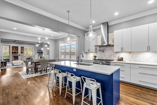 kitchen with a healthy amount of sunlight, sink, wall chimney exhaust hood, and an island with sink