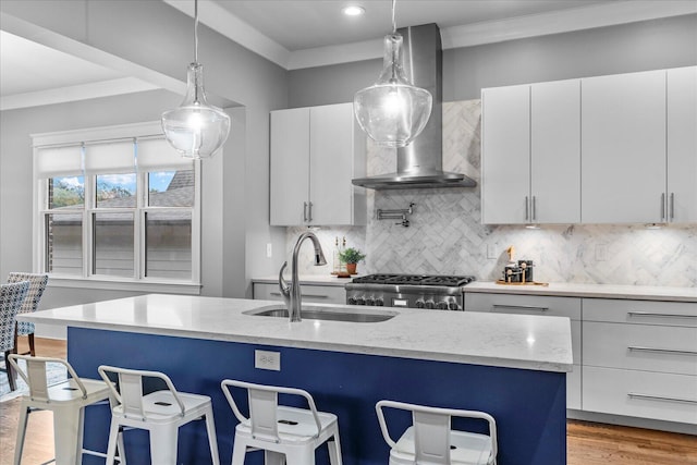 kitchen with wall chimney exhaust hood, a breakfast bar, sink, white cabinetry, and an island with sink