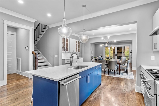 kitchen featuring appliances with stainless steel finishes, blue cabinets, a kitchen island with sink, sink, and hanging light fixtures