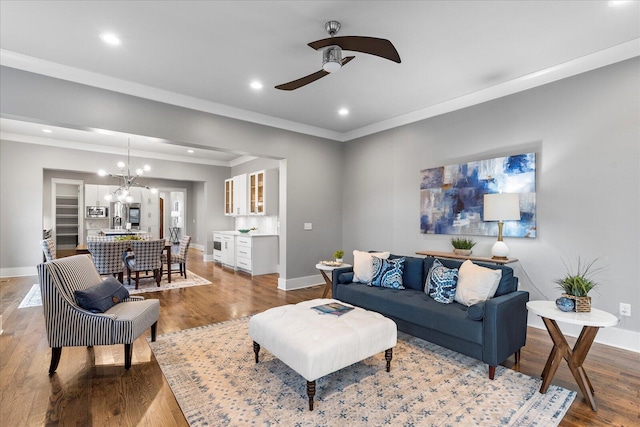 living room featuring ceiling fan with notable chandelier, light wood-type flooring, and crown molding