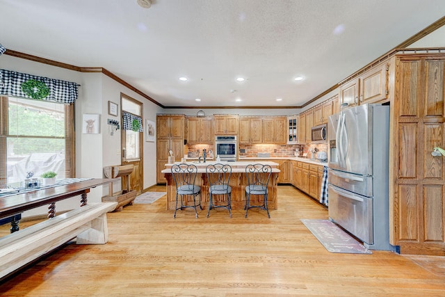 kitchen featuring backsplash, a breakfast bar, stainless steel appliances, a kitchen island with sink, and light hardwood / wood-style flooring