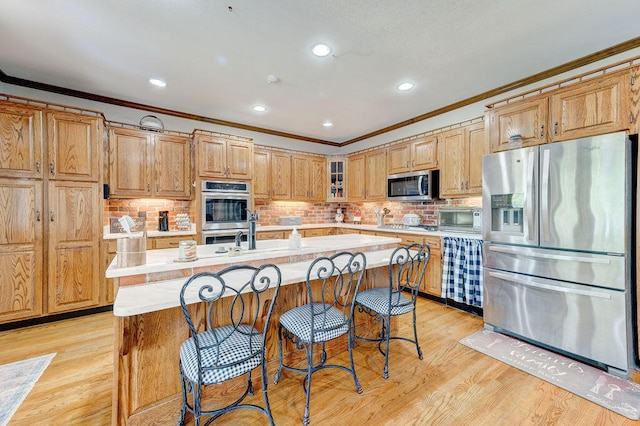 kitchen with stainless steel appliances, light hardwood / wood-style flooring, crown molding, and an island with sink