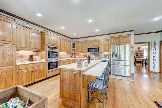 kitchen with stainless steel appliances, light hardwood / wood-style flooring, a kitchen island with sink, and ornamental molding