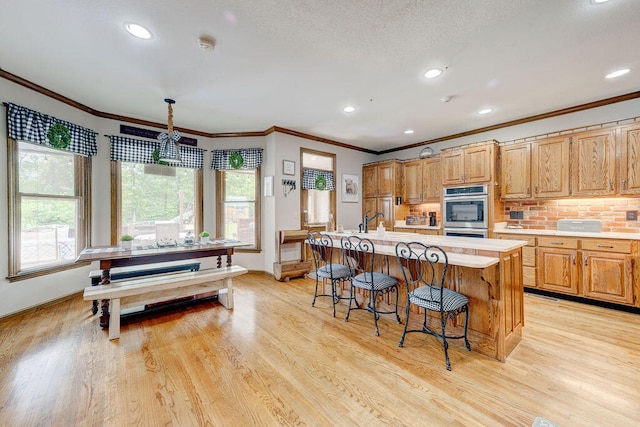 kitchen featuring stainless steel double oven, crown molding, sink, a center island with sink, and light hardwood / wood-style flooring