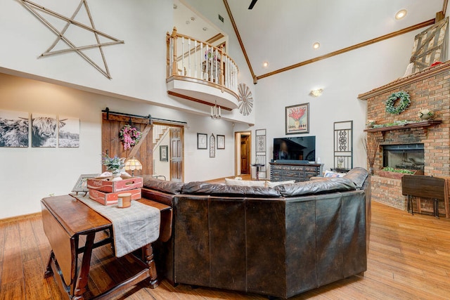 living room featuring a barn door, high vaulted ceiling, crown molding, light hardwood / wood-style floors, and a fireplace