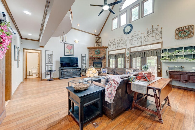 living room with high vaulted ceiling, ceiling fan with notable chandelier, crown molding, a brick fireplace, and light hardwood / wood-style floors