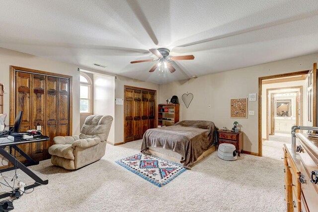 carpeted bedroom featuring ceiling fan, a textured ceiling, and multiple closets