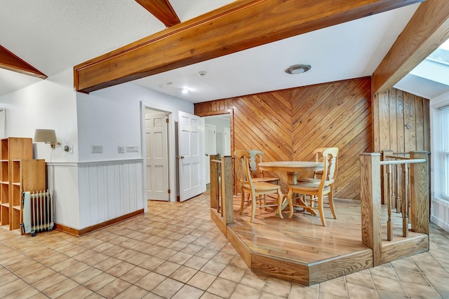 dining area with a textured ceiling, wood walls, radiator, and light tile patterned floors