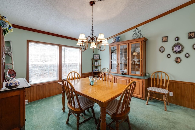 carpeted dining area featuring a textured ceiling, ornamental molding, wooden walls, and a chandelier